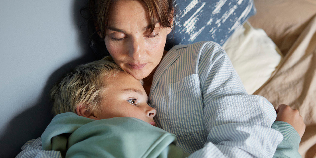 Mamma kramar om sitt barn i sängen.