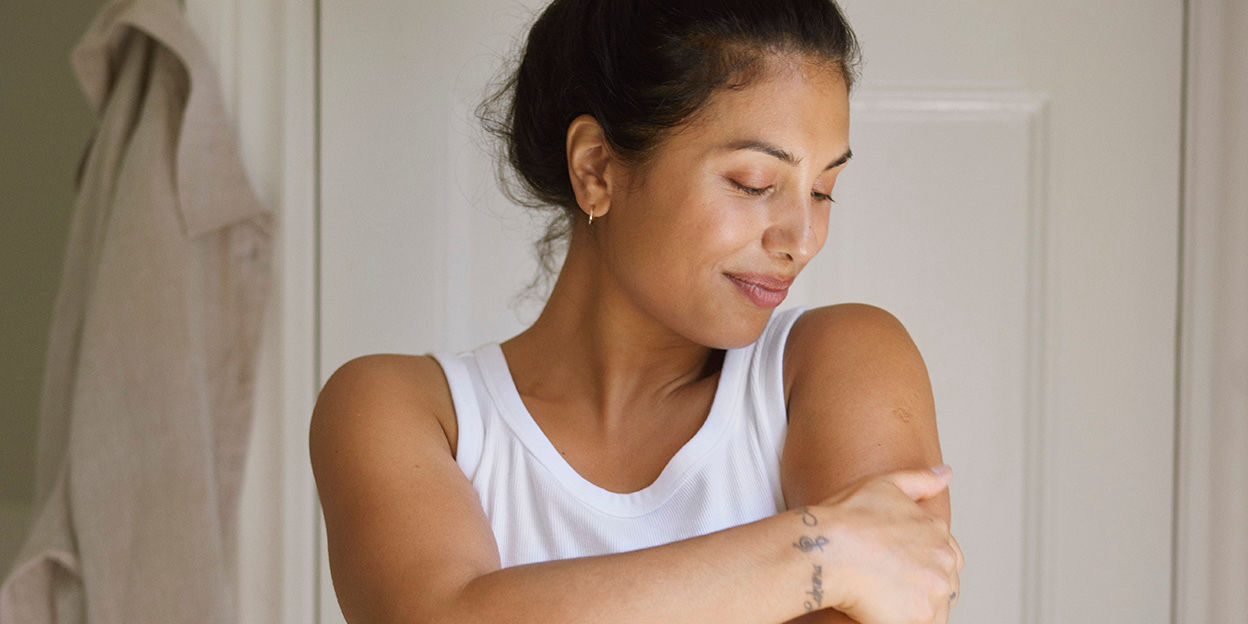 Kvinna håller sig om ena överarmen och tittar ner med ett leende.