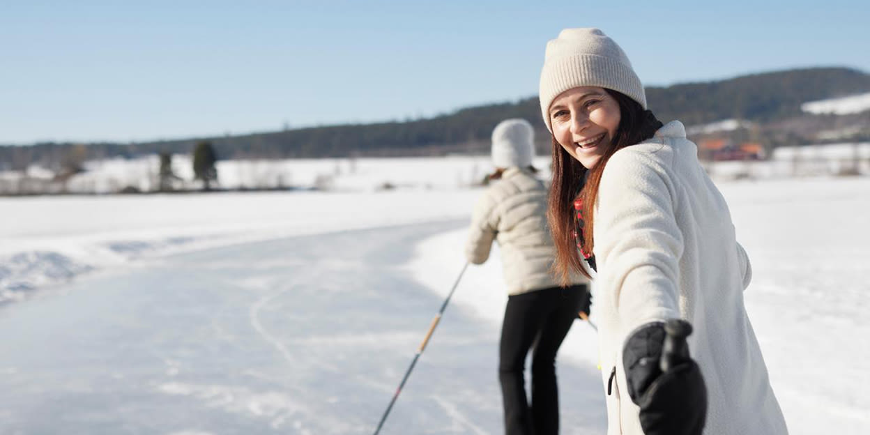 Glad kvinna åker skridskor ute på isen. Solen skiner och hon tittar bakåt och in i kameran.