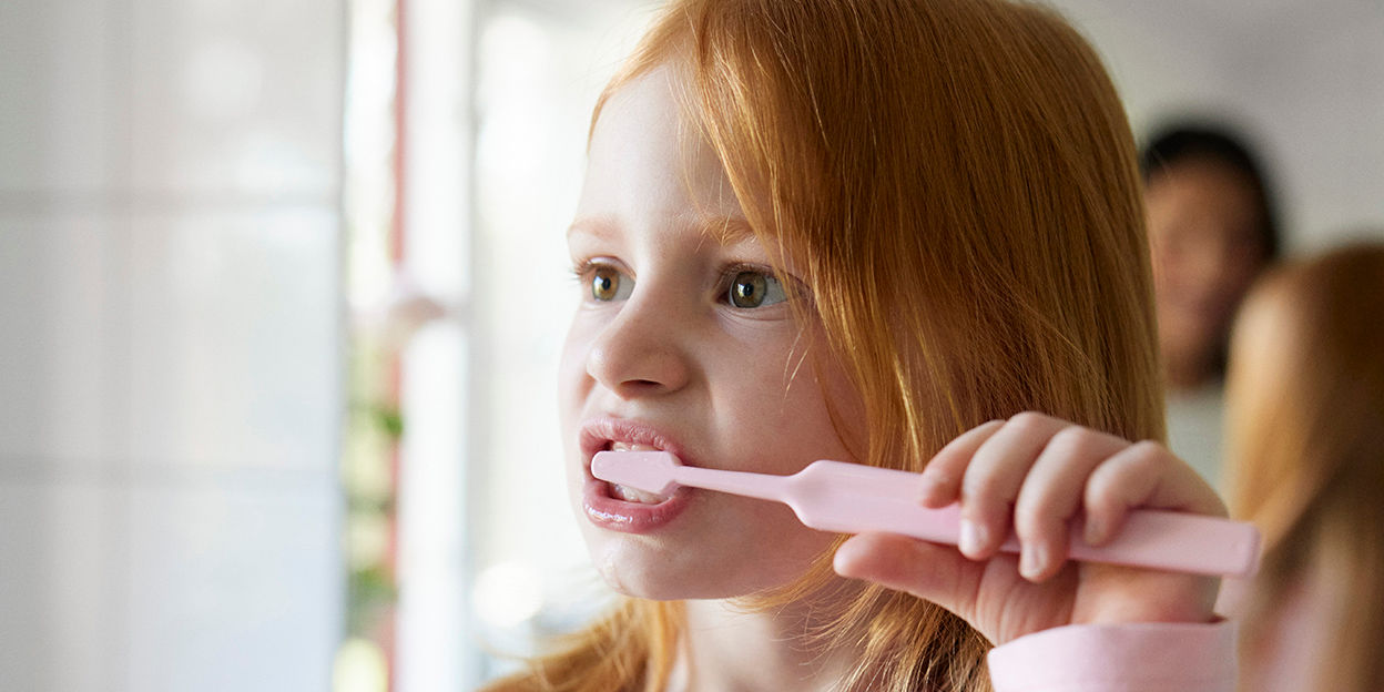 Ett barn borstar tänderna och kollar bort från kameran. 