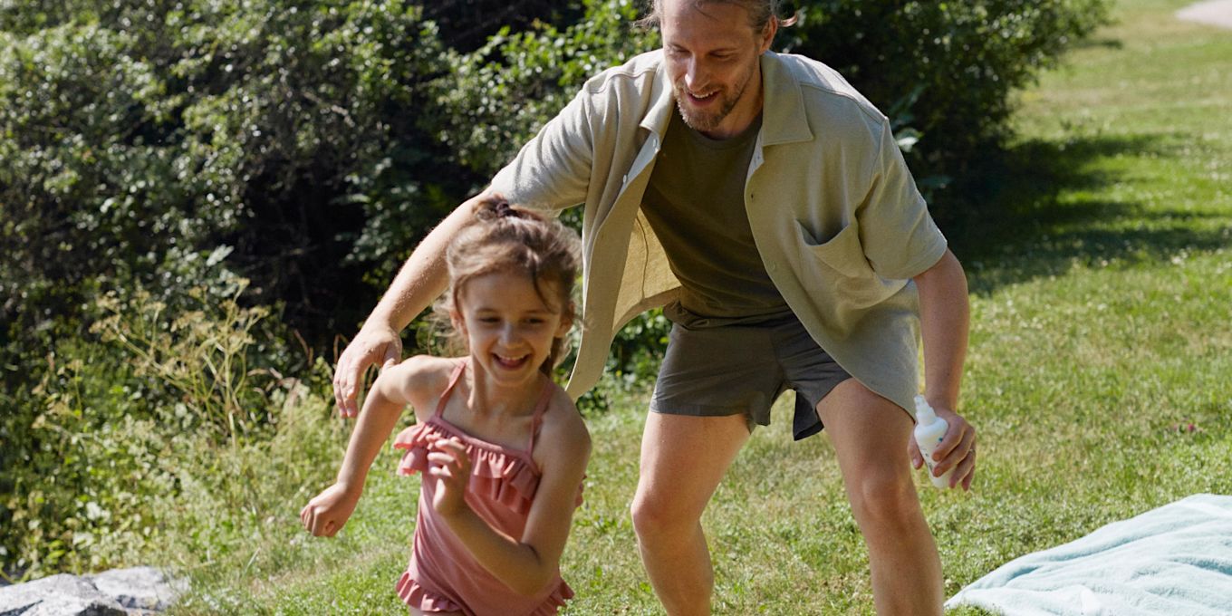 Pappa och dotter leker utomhus i solskenet.