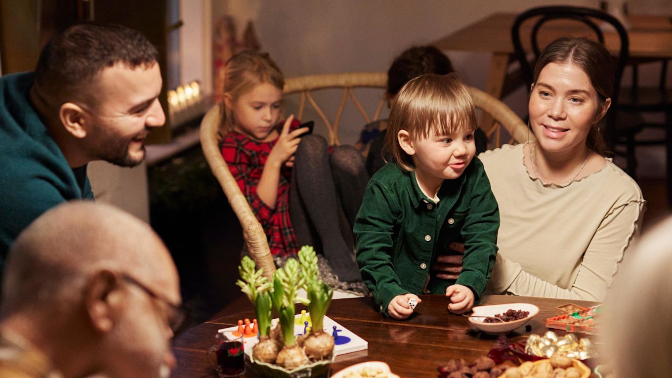 Familj och släkt sitter tillsammans och pratar och fikar runt ett bord på julen.