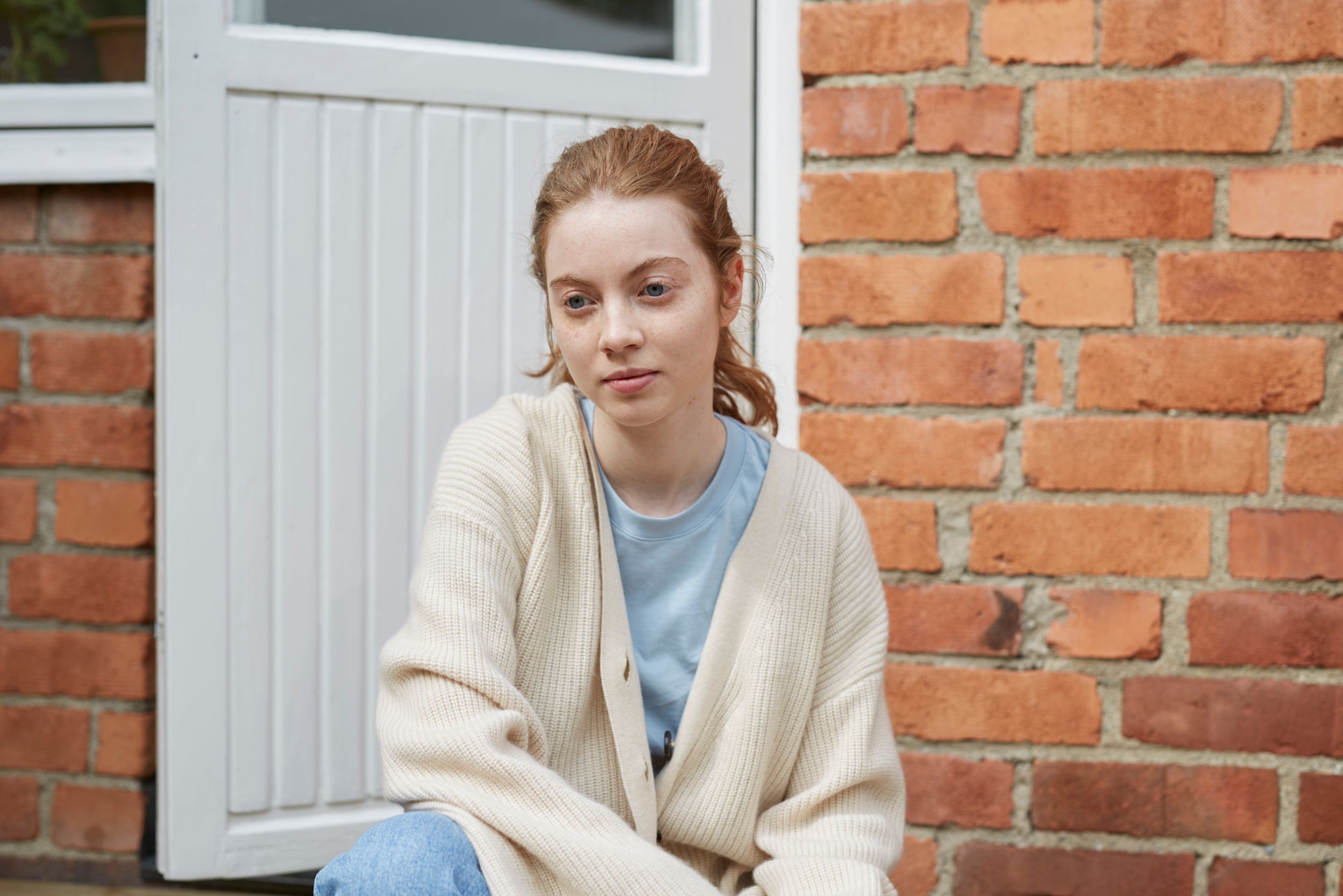 Tjej i tonåren sitter utanför ytterdörren och stirrar med tom blick framför sig.