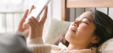 En kvinna ligger i sängen och tittar på en surfplatta.