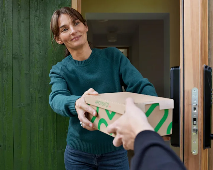 Kvinna står i dörröppningen och tar emot ett paket som hon har beställt med hemleverans.