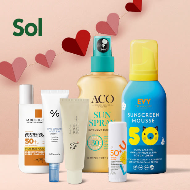 Flera solskyddsprodukter med olika spf-värden står uppradade framför en rosa bakgrund med hjärtformade pappersdekorationer.