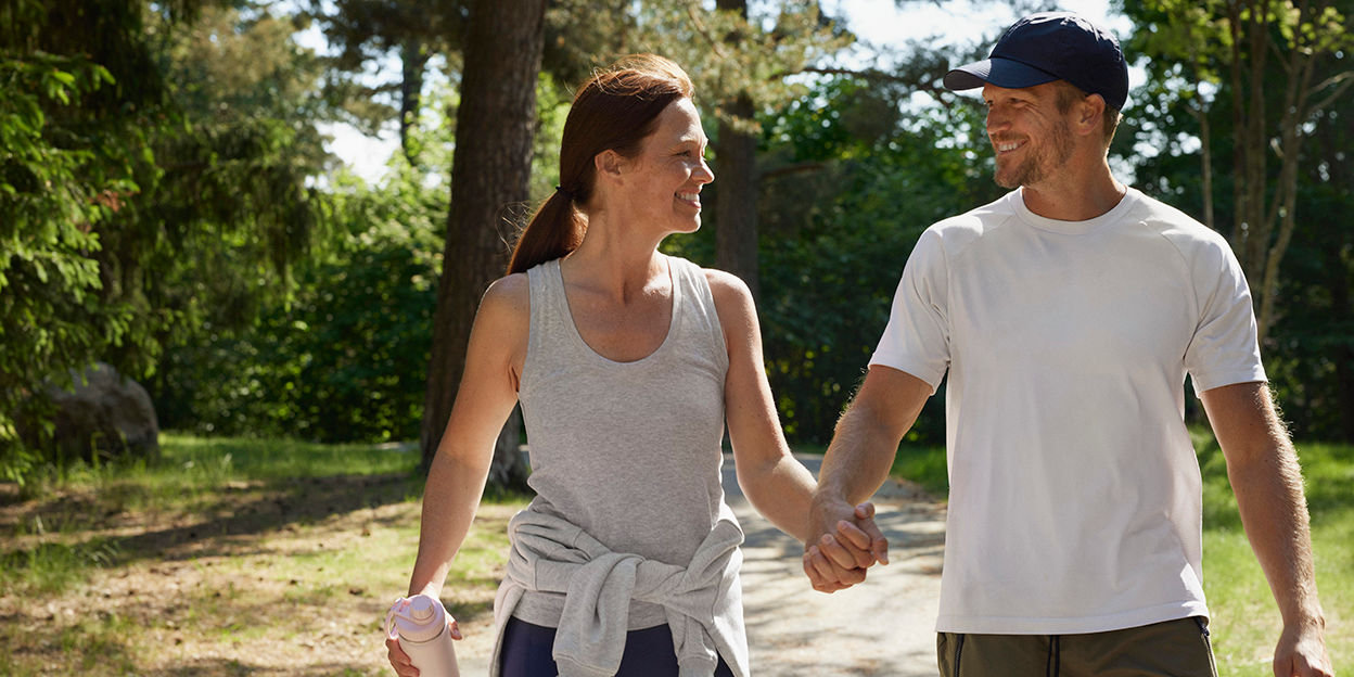 Kvinna och man håller hand och kollar varandra medans de går på en promenad. 