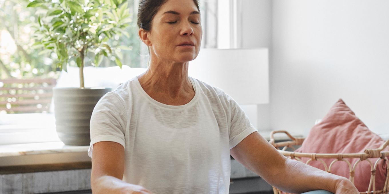 Kvinna sitter på golvet i yogaställning och blundar.
