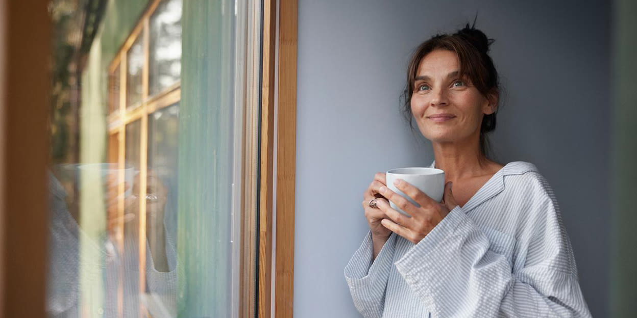 Glad kvinna står med pyjamas och håller i en kopp te.