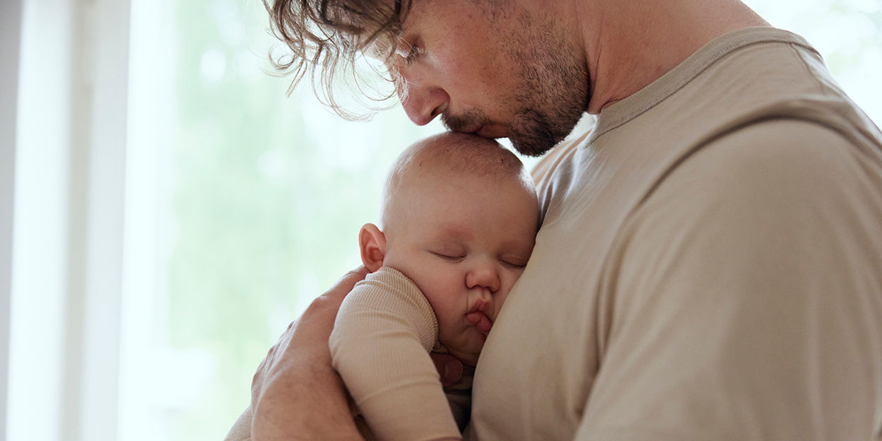 Man håller i bebis och pussar på barnens huvud. 