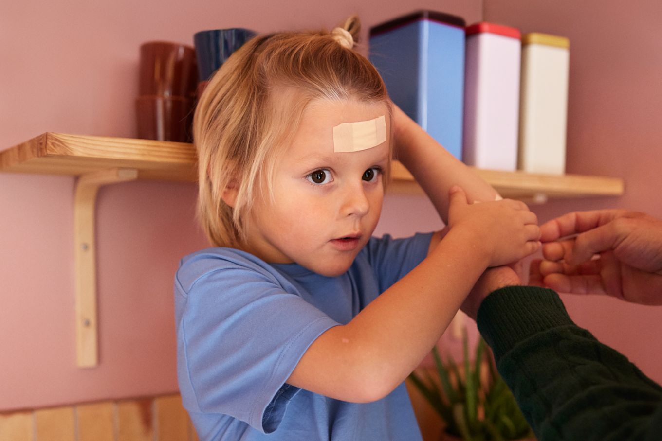 Son har fått ett stort plåster i pannan av sin mamma, sitter på en köksbänk.